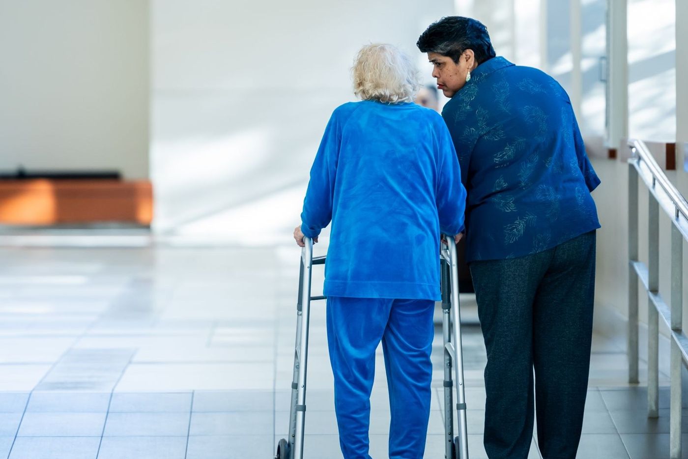 A care assistant walking alongside an elderly patient in a hospital corridor